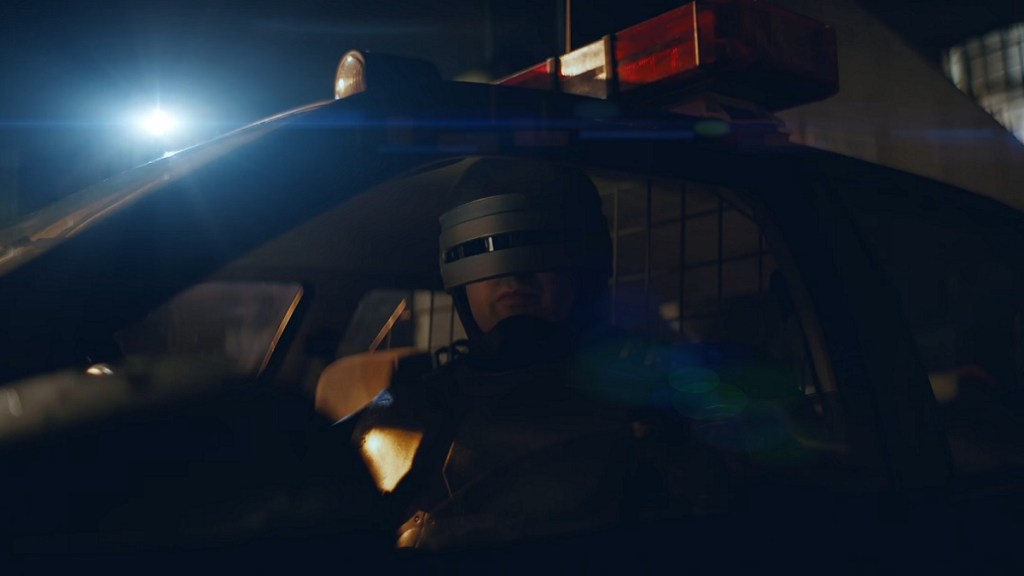 RoboCop sat in the driver's seat of a police car.